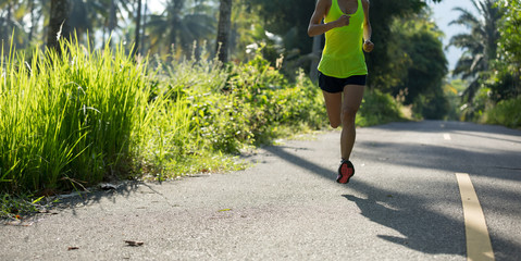 Fototapeta premium Young fitness woman running on morning tropical forest trail