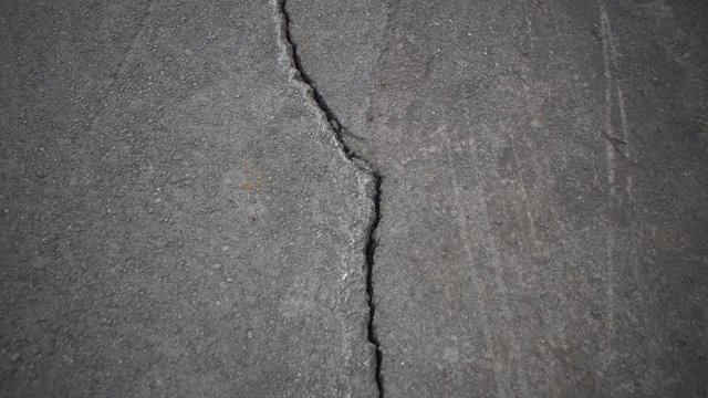 Camera moves along deep cracks in asphalt. View of fault in road, consequences of natural disaster, earthquake or man-made disaster.