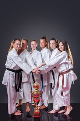 Group of beautiful female karate players posing with the cup on the gray background. Celebrating 1st place.