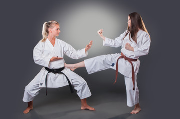 Beautiful young female karate player doing kick on the gray background © cirkoglu