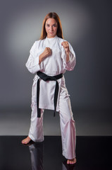 Beautiful young female karate player posing on the gray background © cirkoglu