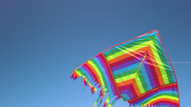 Aquilone con colori dell'arcobaleno che vola in aria con sfondo blu del cielo.