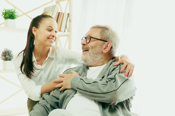 A daughter or granddaughter spends time with the grandfather or senior man. Family or fathers' day, positive emotions and happieness. Lifestyle portrait at home. Two people caddling and smiling.