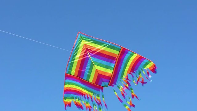 Aquilone con colori dell'arcobaleno che vola in aria con sfondo blu del cielo.