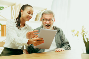 A daughter or granddaughter spends time with the grandfather or senior man. Family or fathers' day, emotions and happieness. Lifestyle portrait at home. Girl taking care about dad. Using a tablet.