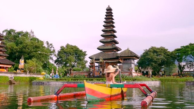 Beautiful girl kayaking on the catamaran at the ulun datu pura bratan temple, in Bali.