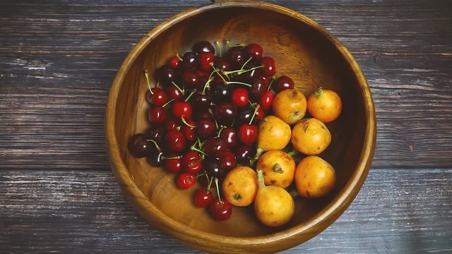 Japanese plum or Japanese medlar and cherries in wooden bowl rotating. Fresh fruits. Vegetarian healthy food concept.