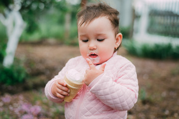 little girl in the garden on the background of greenery and trees very cute eating ice cream finger in a waffle Cup