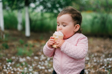 little girl in the garden on the background of greenery and trees very cute eating ice cream in a waffle Cup