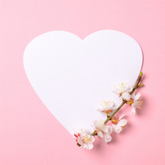 Creative flat lay composition: heart-shaped paper and blooming sakura branch on pink background. Top view, floral round frame, abstract design. Invitation, greeting card or an element for your design