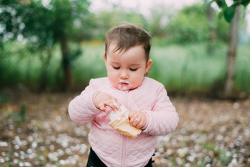 little girl in the garden on the background of greenery and trees very cute eating ice cream finger in a waffle Cup