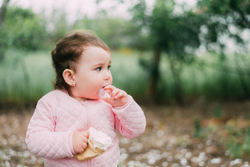 little girl in the garden on the background of greenery and trees very cute eating ice cream finger in a waffle Cup