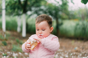 little girl in the garden on the background of greenery and trees very cute eating ice cream finger in a waffle Cup