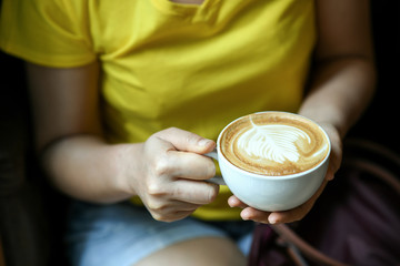 Women's hand holding a cup of latte coffee leaf shaped.