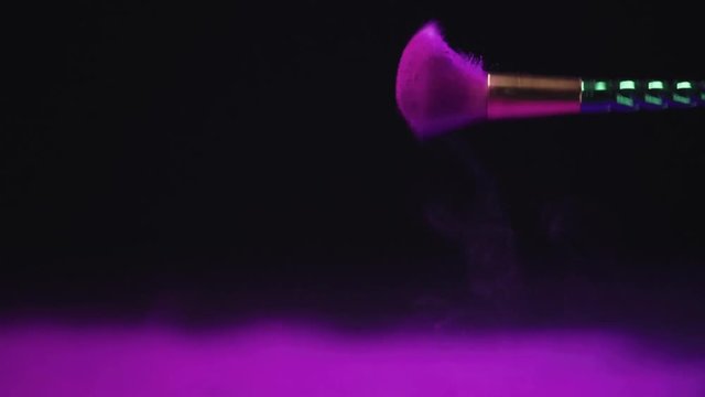 slow motion shoot of bright purple holi paint scattering from cosmetic brush
