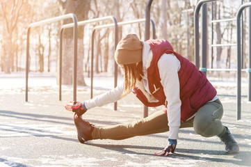 Sports girl in warm clothes on a sunny day does a warm-up on the outdoor sports field in the winter in spring or autumn during the cold season on the background of bars and horizontal bars