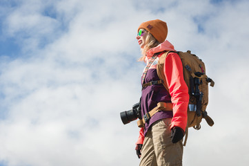 Portrait of a hipster tourist girl photographer with a camera in sunglasses and a hat against the background of blue sky and clouds. Photo travel concept