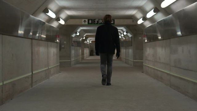 Man walks through subterranean tunnel in subway.One man, alone, walking through an empty concrete subterranean pedestrian tunnel  lines with lights and reflective metal. It is under a GO train station