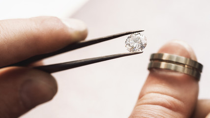 Jeweler tries on a gemstone next to a gold blank for the future ring, close-up