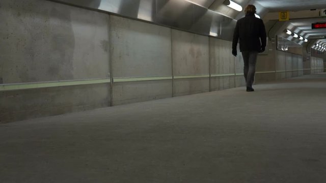 Man walks through subterranean tunnel in subway.One man, alone, walking through an empty concrete subterranean pedestrian tunnel  lines with lights and reflective metal. It is under a GO train station