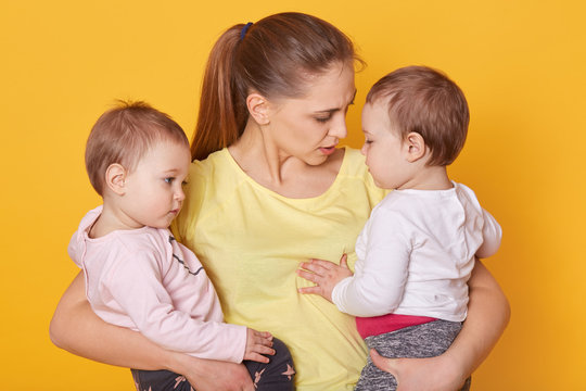 Image of mother with her sweet children, posing in studio. Mummy and girls twins, dressed casually, mom tells her doughters about Mother's Day. Little children listen to mommy story and hugging her.