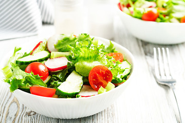 Salad in a white ceramic bowl on a white wooden background