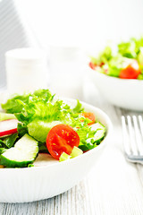 Salad in a white ceramic bowl on a white wooden background