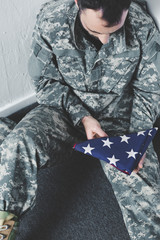 high angle view of depressed man in military uniform sitting on floor in corner and holding usa national flag