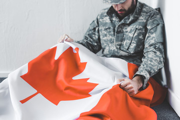 depressed man in military uniform sitting on floor in corner and holding canada national flag