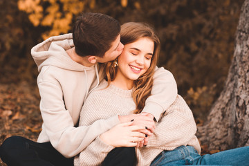 Happy love couple og teenagers sitting under tree outdoors. Boy kissing girl. Teenagerhood.