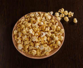 A plate of popcorn is on the table. Pieces of popcorn scattered on the table.