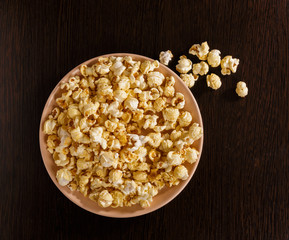 A plate of popcorn is on the table. Pieces of popcorn scattered on the table.