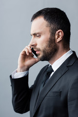 thoughtful, handsome bearded man in black suit using smartphone and looking down