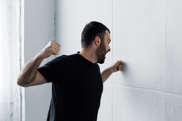 angry bearded man in black t-shirt screaming and kicking white wall