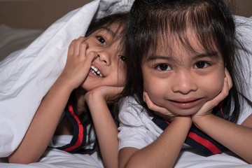 Fototapeta na wymiar happy little girls twins sister in bed under the blanket having fun, smiling and wacky
