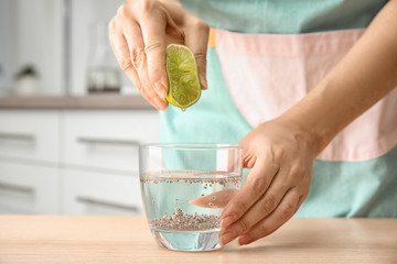 Young woman squeezing lime into glass of water with chia seeds on table, closeup