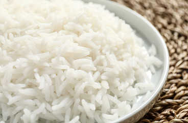 Plate of tasty cooked rice on wicker mat, closeup