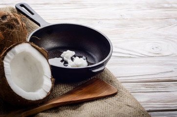 Coconut, shell with meat, cast iron skillet and spatula on hemp sackcloth on white wooden kitchen...