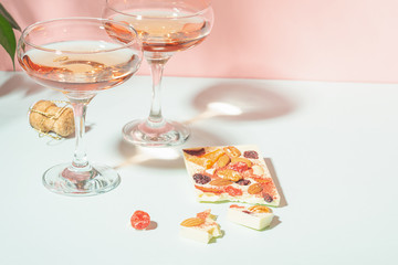Drink champagne or wine in two elegant glasses and a bar of white chocolate. Gentle pink background bright sunlight.