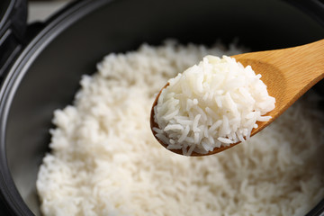 Spoon with tasty hot rice over cooker, closeup