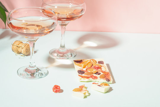 Drink champagne or wine in two elegant glasses and a bar of white chocolate. Gentle pink background bright sunlight.