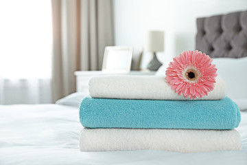 Stack of clean towels with flower on bed indoors. Space for text