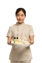 Professional masseuse in uniform holding tray with spa supplies on white background