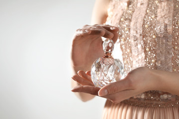 Young woman with bottle of perfume on light background, closeup. Space for text - obrazy, fototapety, plakaty