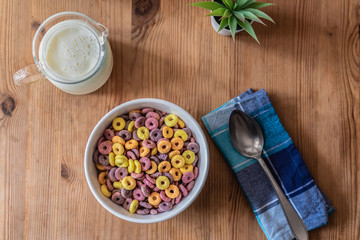 Mesa de madera con cuenco de cereales, leche en jarra, servilleta y cuchara.