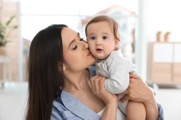 Happy young mother kissing her adorable baby in living room