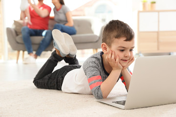 Boy with laptop lying on carpet near his family at home