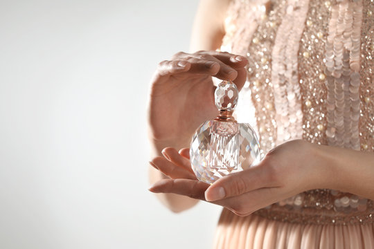 Young woman with bottle of perfume on light background, closeup. Space for text