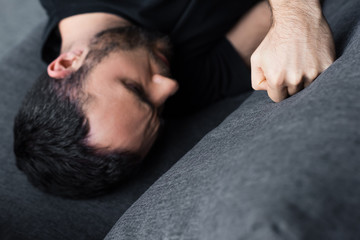 overhead view of depressed man lying on sofa and kicking it with fist