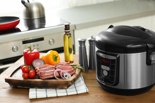 Modern multi cooker and products on wooden table in kitchen